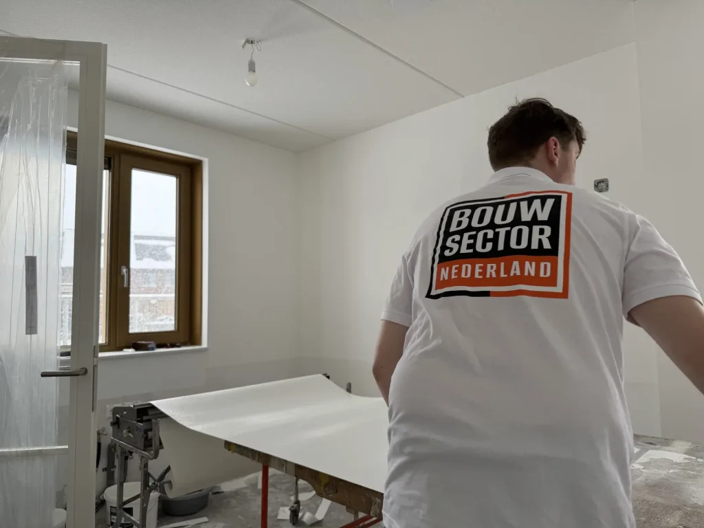 Behanger van Bouwsector Nederland rolt een baan renovlies uit over de plaktafel in een kale nieuwbouwkamer