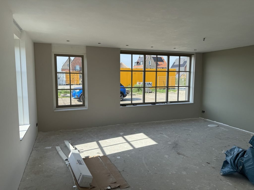 Lege nieuwbouwkamer met een wand in een warme grijstint en grote ramen