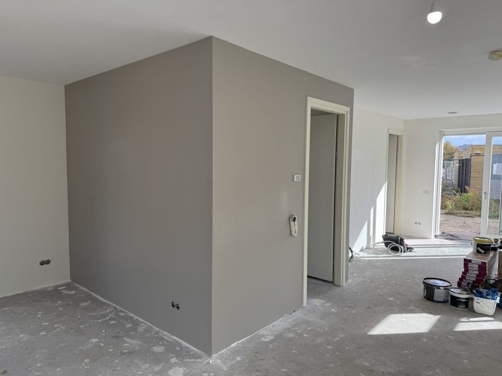 Nieuwbouwwoning met een pas afgewerkte grijze wand en verfemmers op de kale vloer